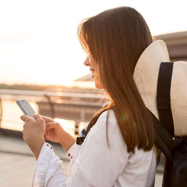 Side view of woman with hat using smartphone while traveling alone