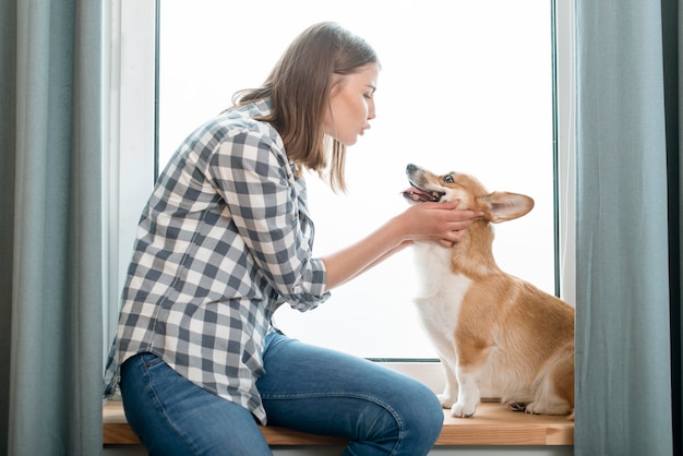 Vista laterale della donna con il suo cane davanti alla finestra