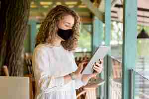Free photo side view woman with mask using tablet