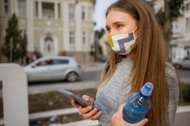 Side view woman with medical mask holding a bottle of water