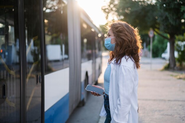 Вид сбоку на женщину с медицинской маской, ожидающую, пока общественный автобус откроет двери