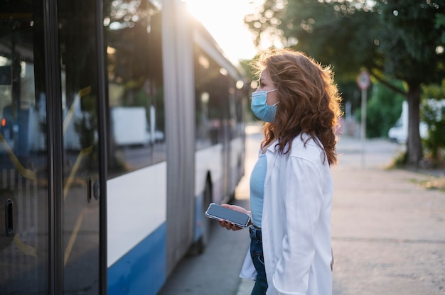 Side view of woman with medical mask waiting for the public bus to open doors