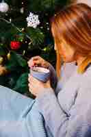 Foto gratuita vista laterale della donna con tazza accanto all'albero di natale