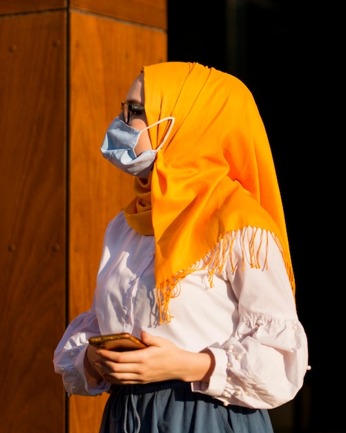 Free photo side view woman with phone and mask