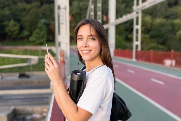 Вид сбоку женщины со смартфоном на мосту во время путешествия