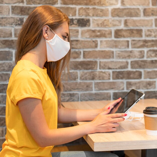 Side view woman with tablet wearing mask