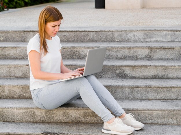 Side view of woman working on laptop outdoors on steps