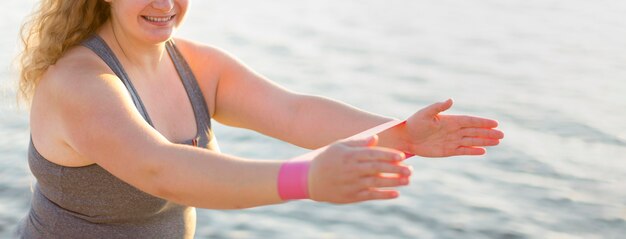 Side view of woman working out by the lake with elastic bands