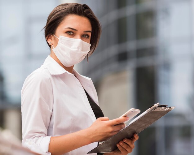 Side view of woman working during pandemic with smartphone and notepad