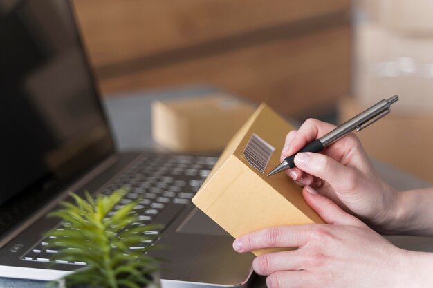 Side view of woman writing on box with laptop and plant