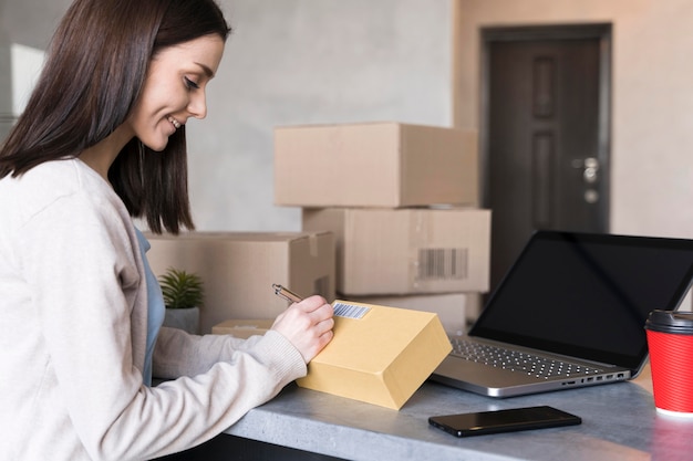 Free photo side view of woman writing on box at work