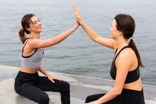 Вид сбоку на женщин, дающих друг другу пять во время тренировки на открытом воздухе