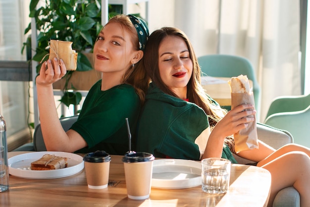 Free photo side view women holding  paper-wrapped sandwich