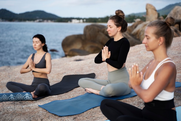 side view women meditating together on beach