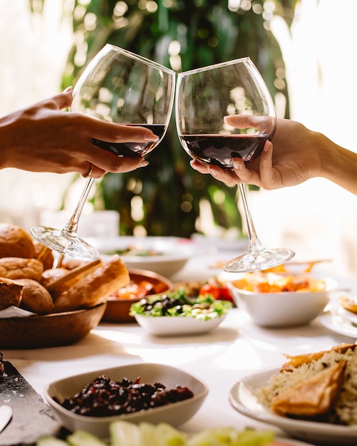Вид сбоку женщин тостов с бокалами красного вина в ресторане