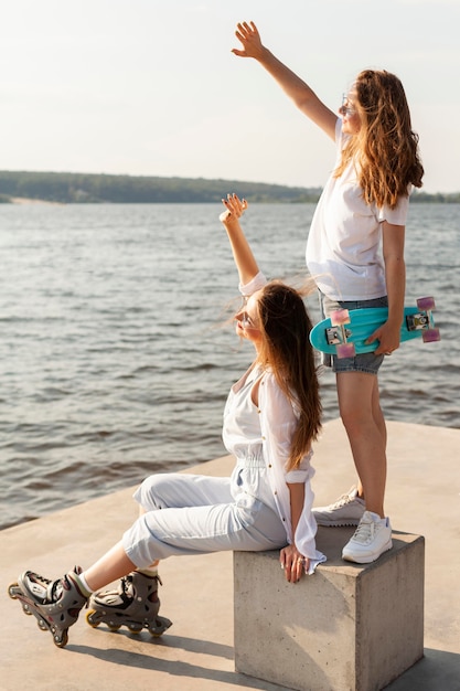 Side view of women with roller blades and skateboard by the lake