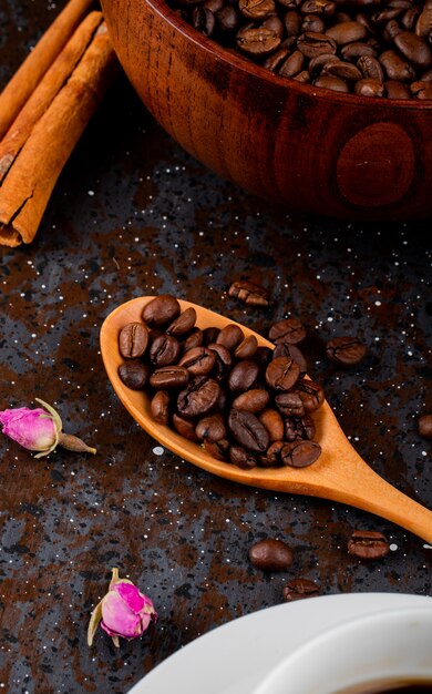 Side view of a wooden spoon with coffee beans on black background