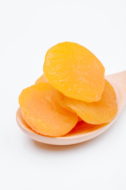 Side view of a wooden spoon with dried apricots on white background