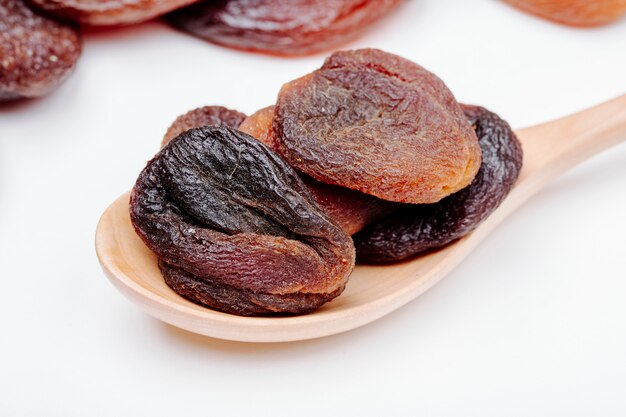 Side view of a wooden spoon with dried apricots on white background