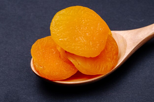 Free photo side view of a wooden spoon with sweet dried apricots on black background