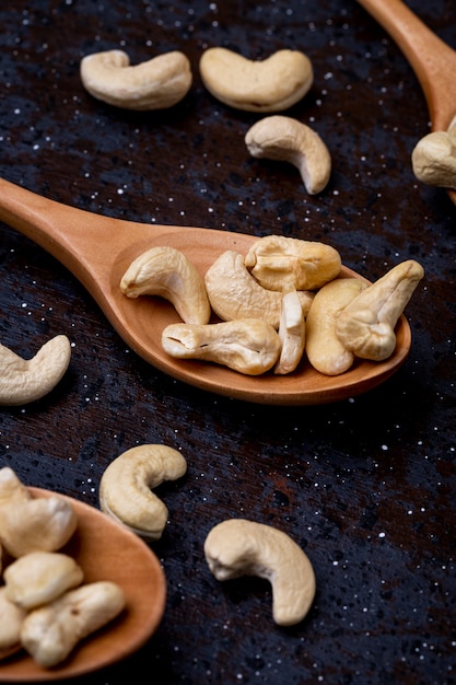 Side view of wooden spoons with cashews on black background