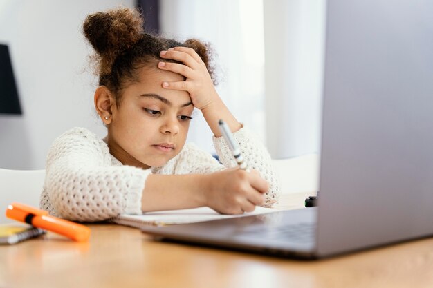 Side view of worried little girl at home during online school with laptop