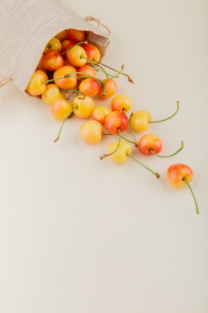 Side view of yellow cherries spilling out of sack on white surface with copy space