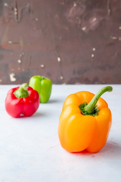 Side view of yellow pepper with other peppers on white surface and maroon background with copy space