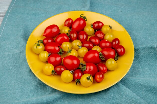 Вид сбоку желтых и красных помидоров в пластине на синей поверхности ткани