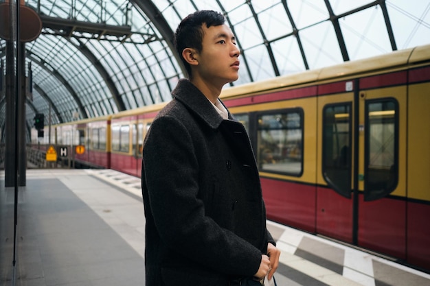 Free photo side view of young asian businessman in coat thoughtfully waiting train at city subway station