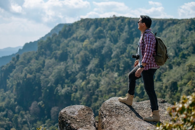 Side view young asian hiking man standing and riseup hands with happy on peak of rocky mountain beautiful landscape in background copy space