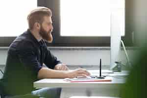 Free photo side view of a young bearded man sitting at his desk
