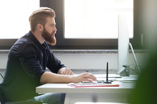 Side view of a young bearded man sitting at his desk