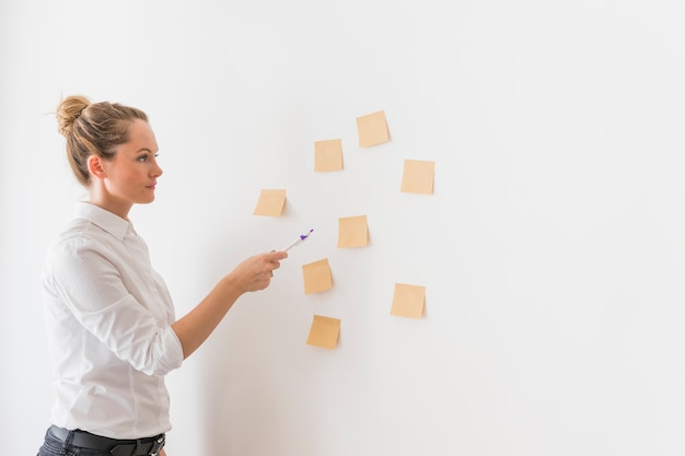 Side view of young business woman pointing toward stick notes on wall