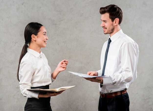 Side view of a young businessman and businesswoman discussing the project standing against grey wall