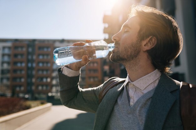 Side view of young businessman refreshing himself and drinking water in the city