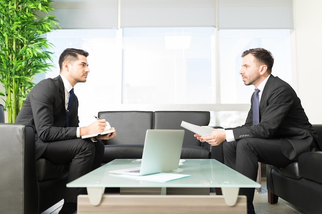 Side view of young businessman taking notes from boss at entrance hall