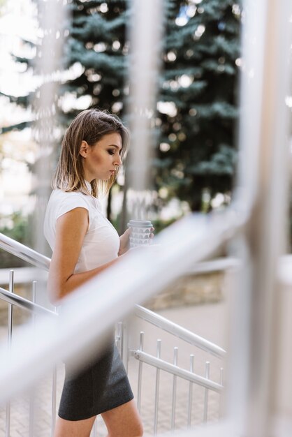 Foto gratuita vista laterale di giovane donna di affari che tiene la tazza di caffè asportabile che sta vicino all'inferriata