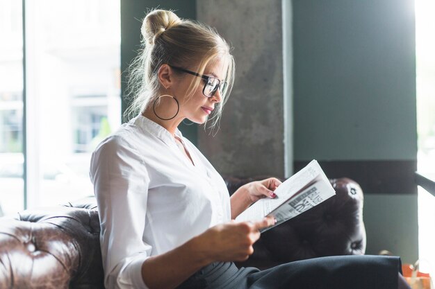 Side view of a young businesswoman reading newspaper in cafe