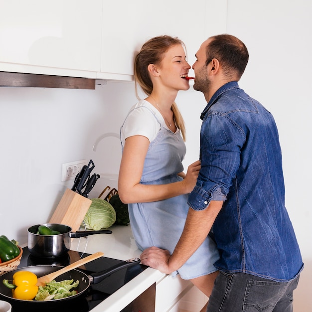 台所でニンジンを一緒に食べる若いカップルの側面図