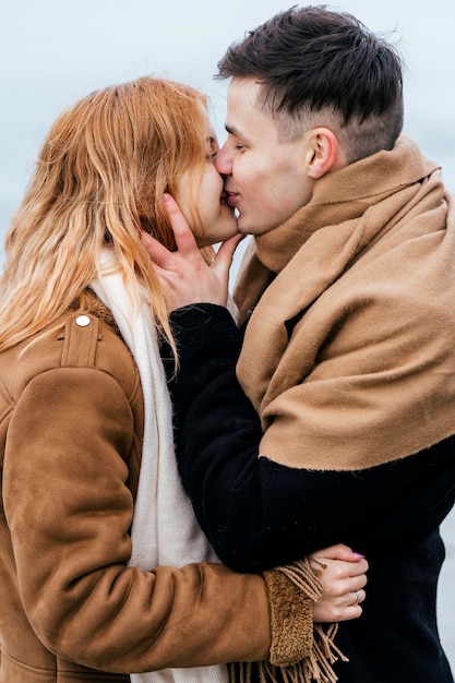 Вид сбоку молодой пары, целующейся зимой
