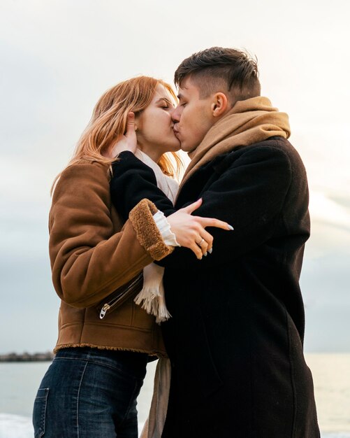 Side view of young couple in winter by the beach kissing