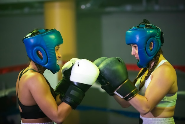 Vista laterale di giovani sparring partner femminili sull'anello. due ragazze forti con i caschi, che si battono le mani nei guanti pronte per iniziare l'incontro, guardandosi seriamente. stile di vita sano, concetto di sport estremo