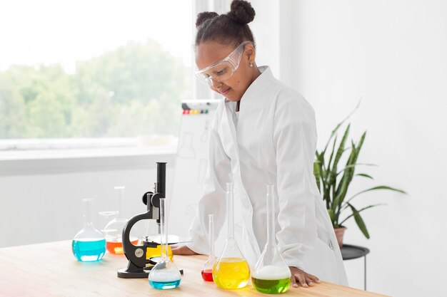 Side view of young girl scientist in lab coat looking at microscope