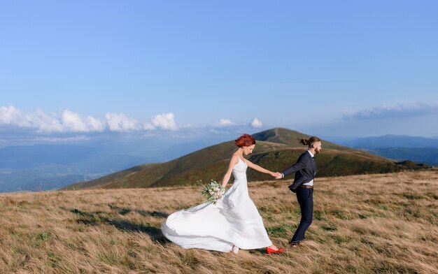 야외에서 걷는 흰 드레스에 빨간 머리 소녀와 젊은 남자의 측면보기