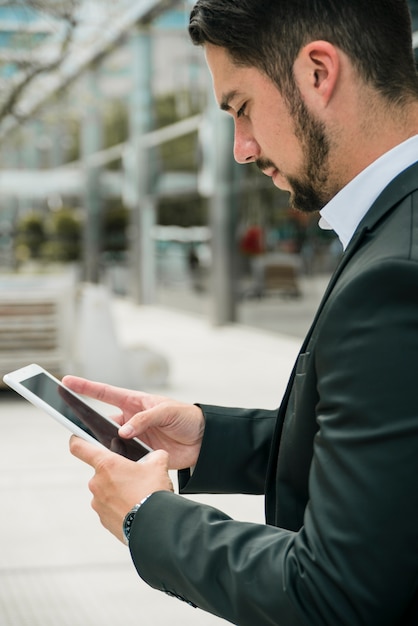 Vista laterale di giovane uomo d'affari bello che per mezzo dello smart phone contro il contesto della sfuocatura