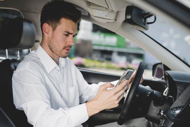 Side view of young handsome man using cell phone in car