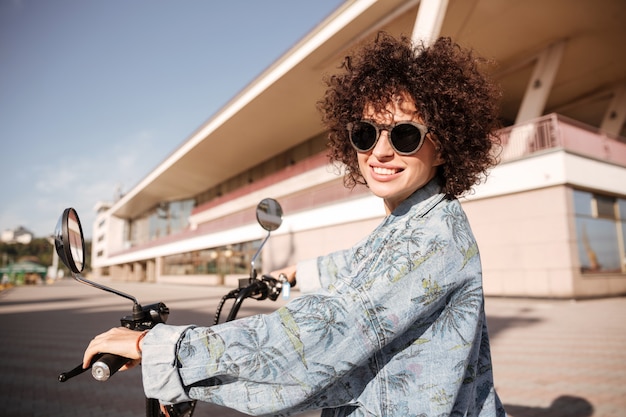 Free photo side view of young happy curly woman in sunglasses posing