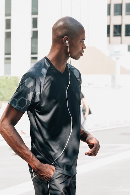 Free photo side view of a young male athlete with hand in his pocket listening music on earphones