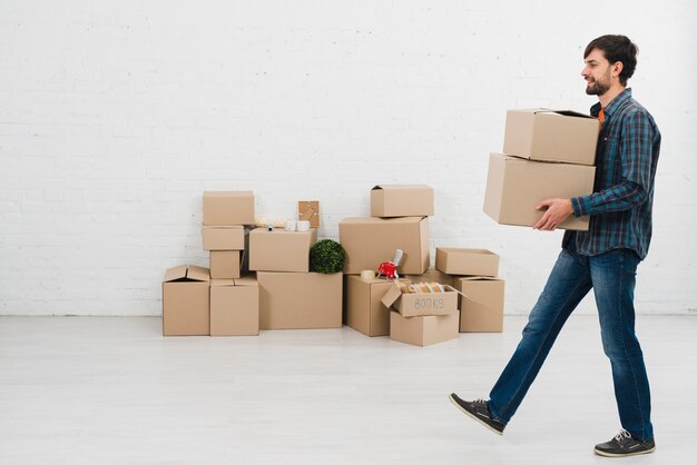 Side view of a young man carrying cardboard boxes in hand walking in room